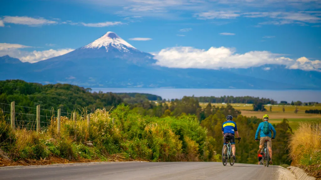 Cyclists ride towards snow-capped Osorno Volcano with Lake Llanquihue in the distance
