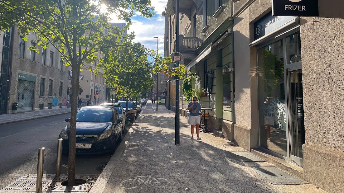Cycle path alongside parked cars and shops in Ljubljana city centre with afternoon sun