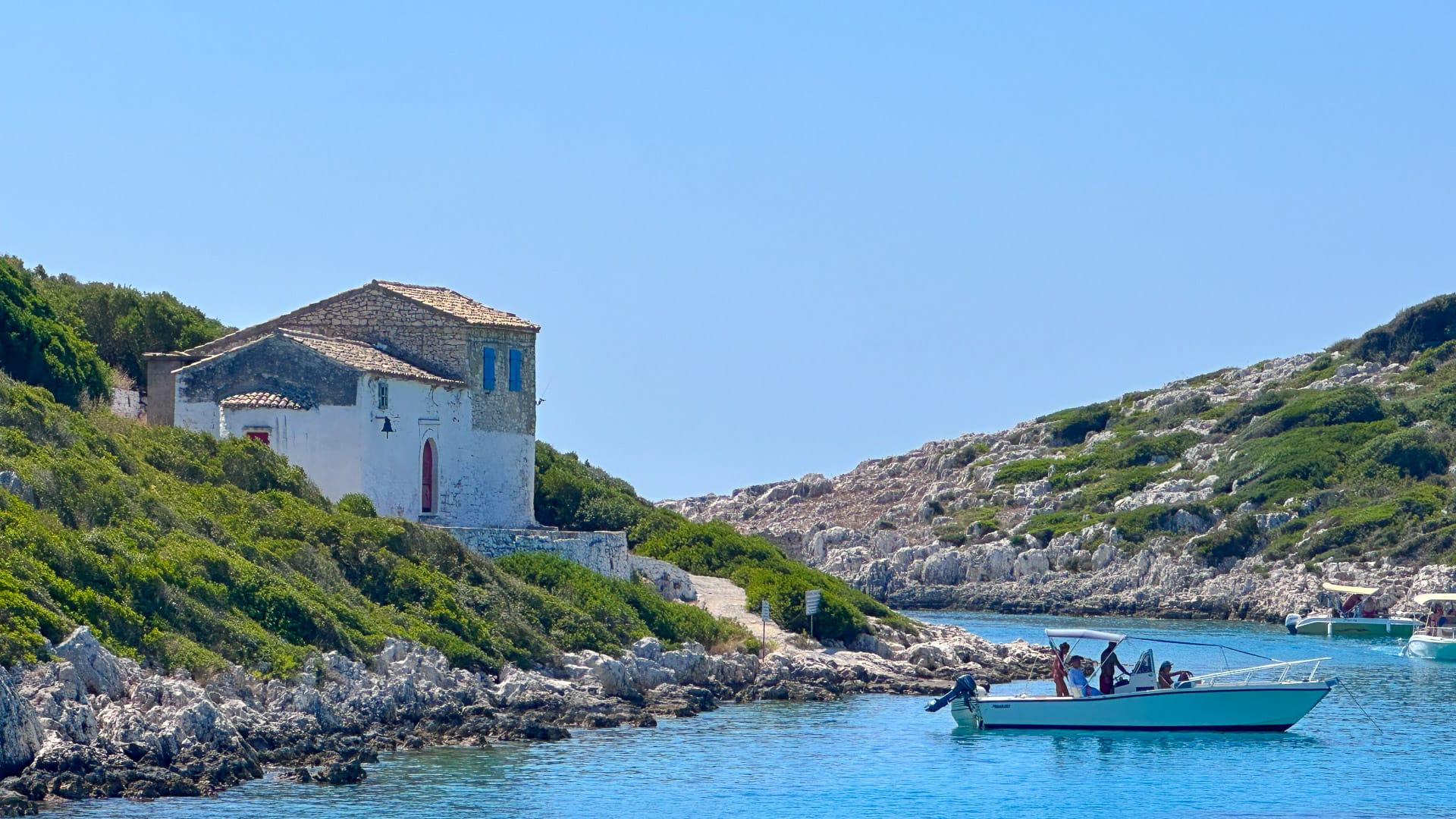 Small boat approaching a stone house by the rocky shoreline of Paxos island in Greece
