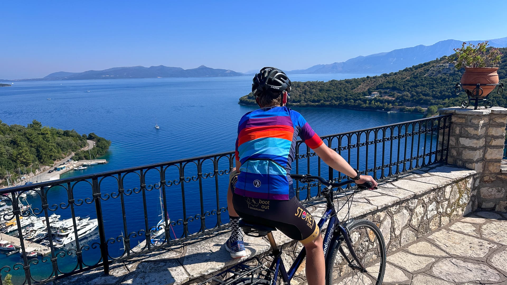 Cyclist overlooking a harbour and blue sea from a stone terrace on Meganisi