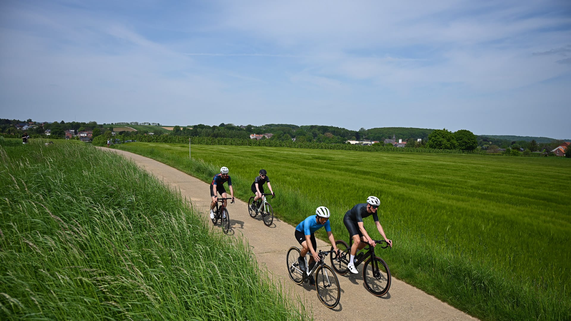Cyclists riding along a rural path surrounded by green fields on the Eddy Merckx Cycling Route in Flanders