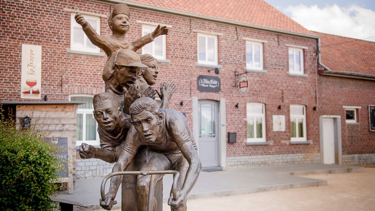 Statue of Eddy Merckx with children celebrating cycling heritage outside a brick café in Flanders