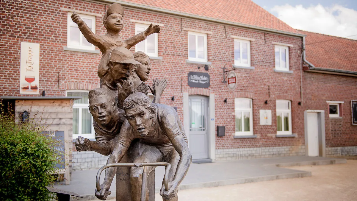 Statue of Eddy Merckx with children celebrating cycling heritage outside a brick café in Flanders