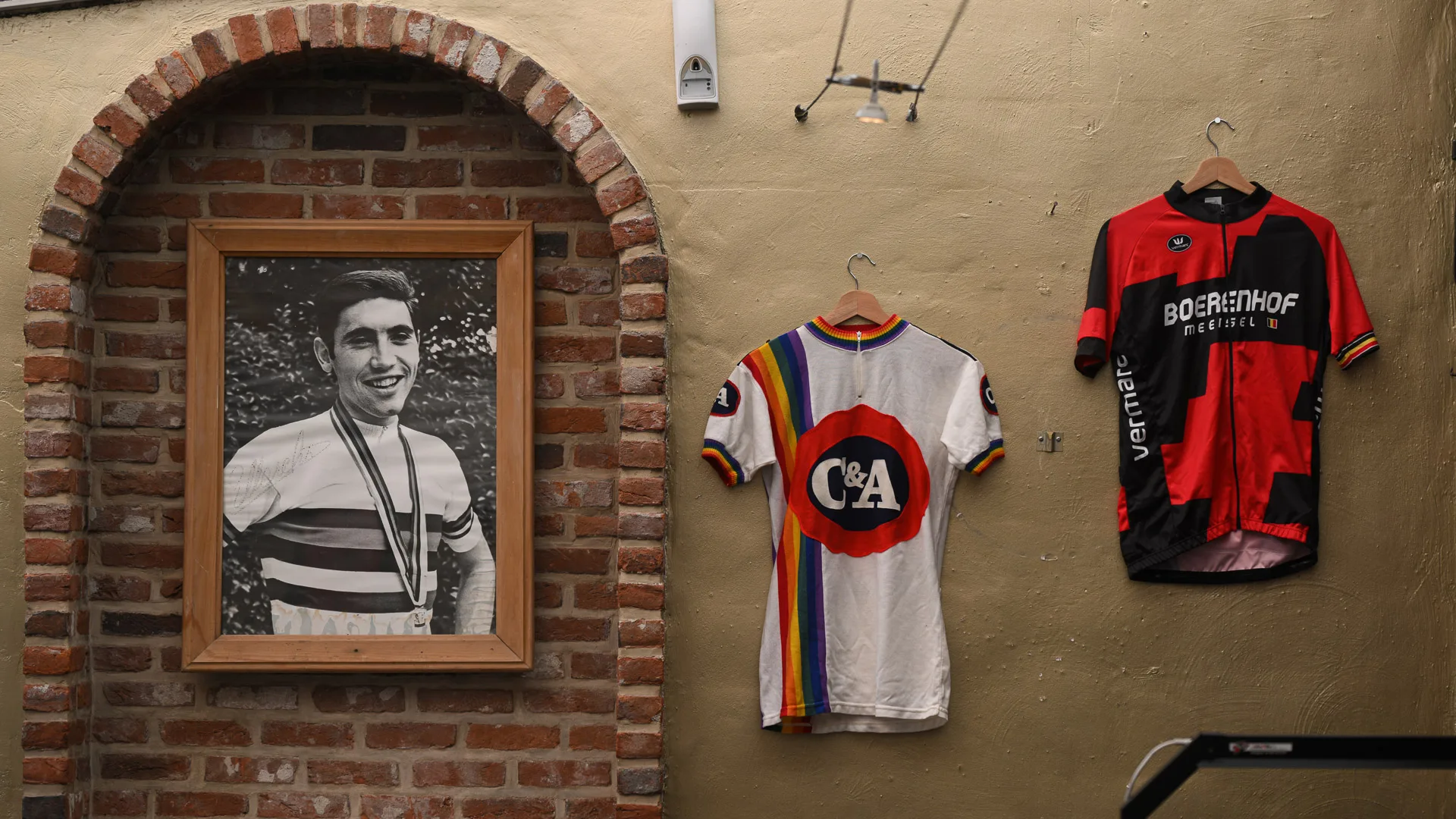 Display of Eddy Merckx memorabilia with cycling jerseys and portrait at café stop in Flanders