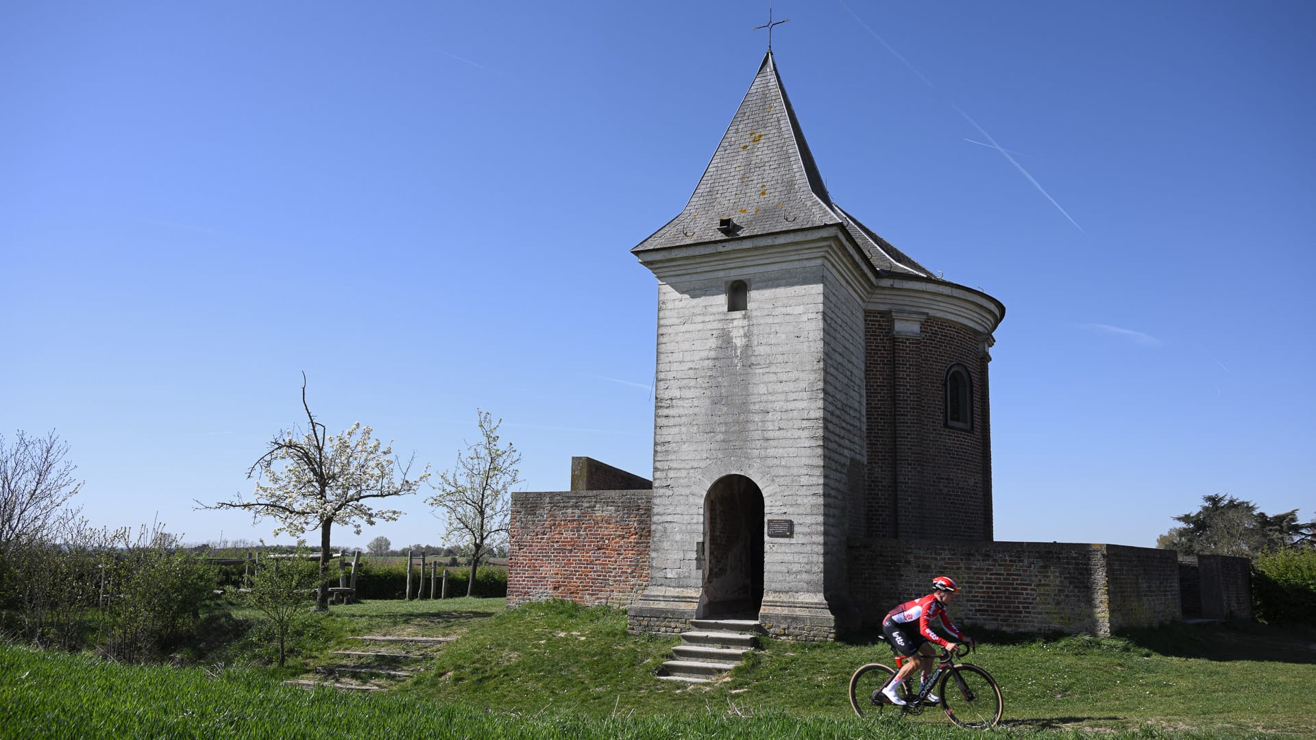 Cyclist passing a small historic chapel on a rural road in Flanders