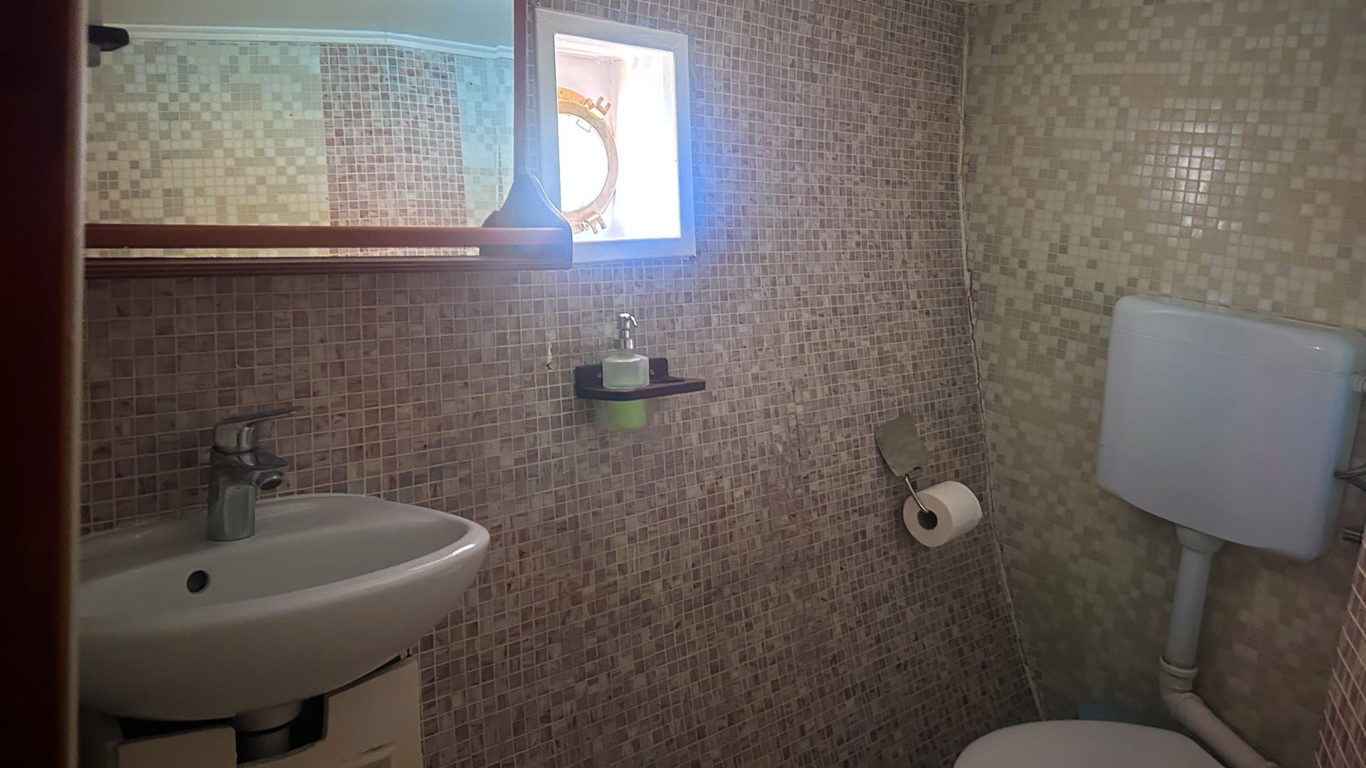 Small tiled bathroom on a wooden boat with sink, mirror and toilet