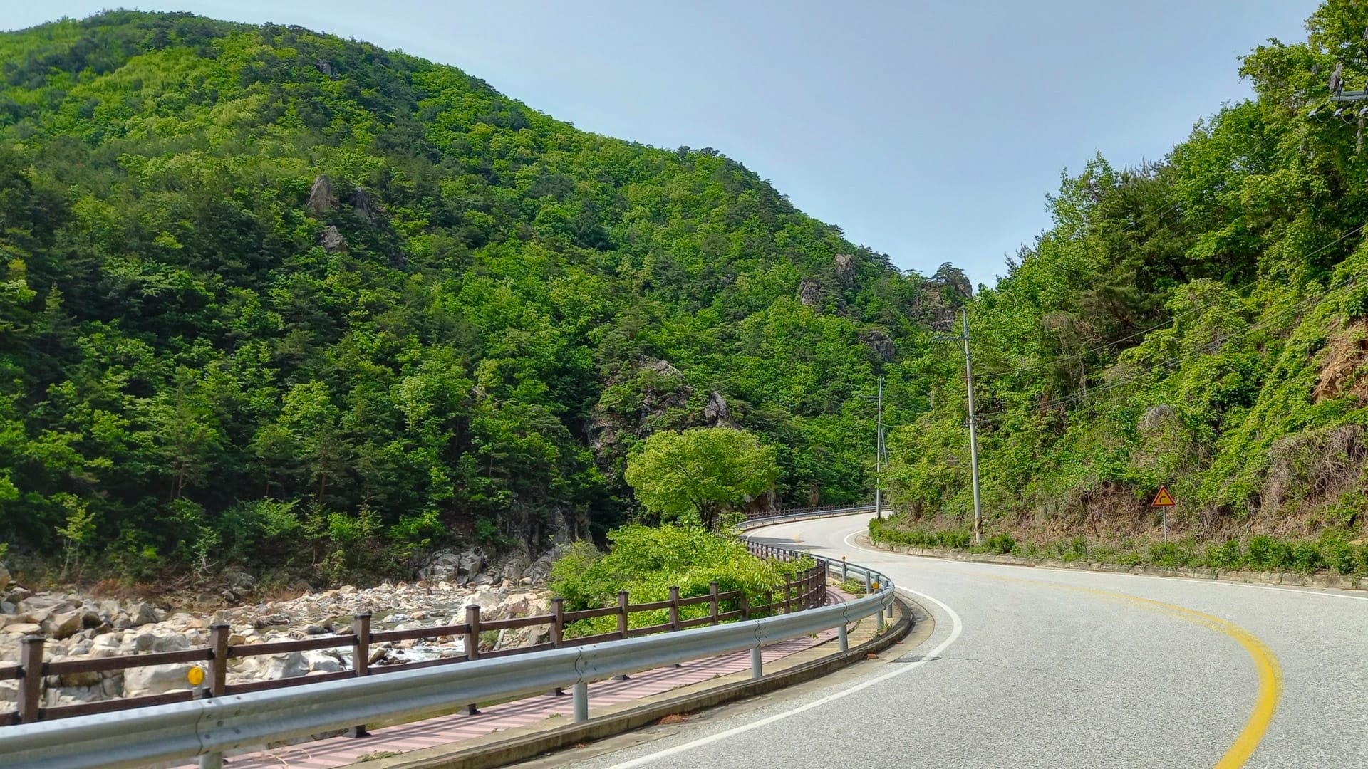 Curving mountain road through lush green hills beside a rocky river in Juwangsan National Park, Korea