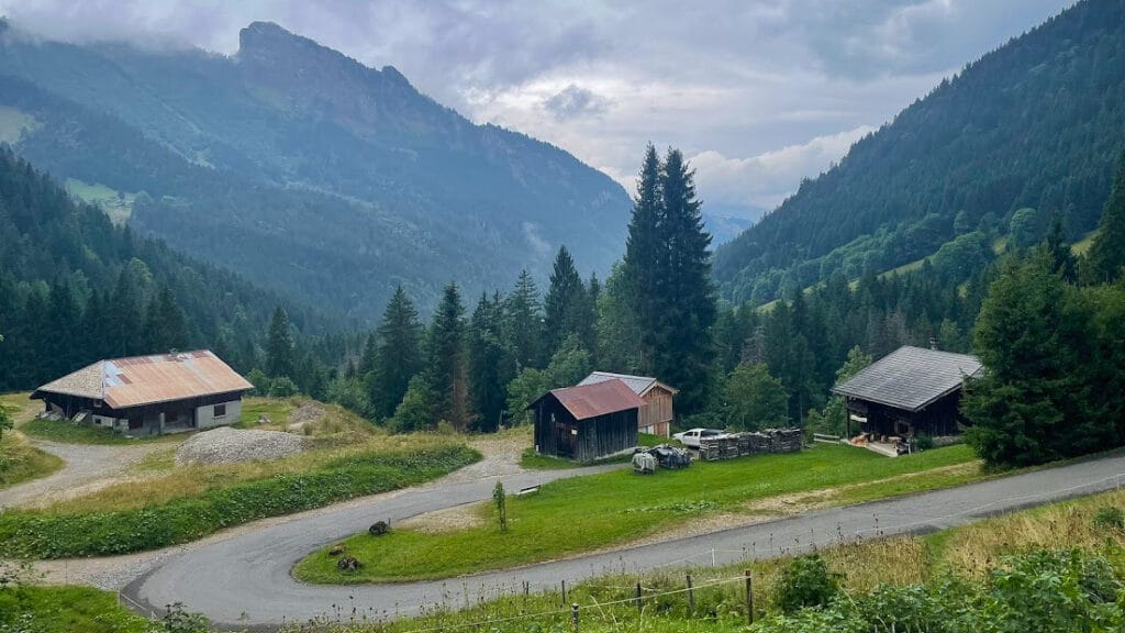 Winding mountain road past alpine chalets on the scenic climb to Lac de Mines d’Or under a cloudy sky