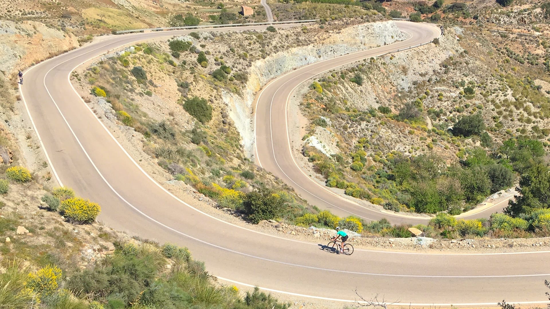 Cycling Andalucia with cyclist on long snaking road through Almeria