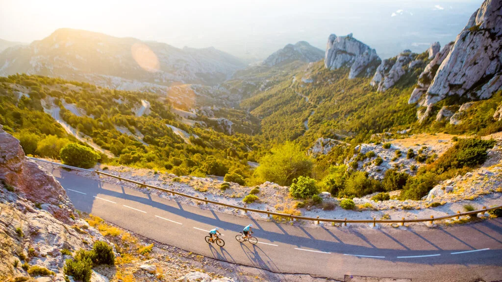 Cyclists descending a winding mountain road through dramatic limestone peaks in southern Catalonia