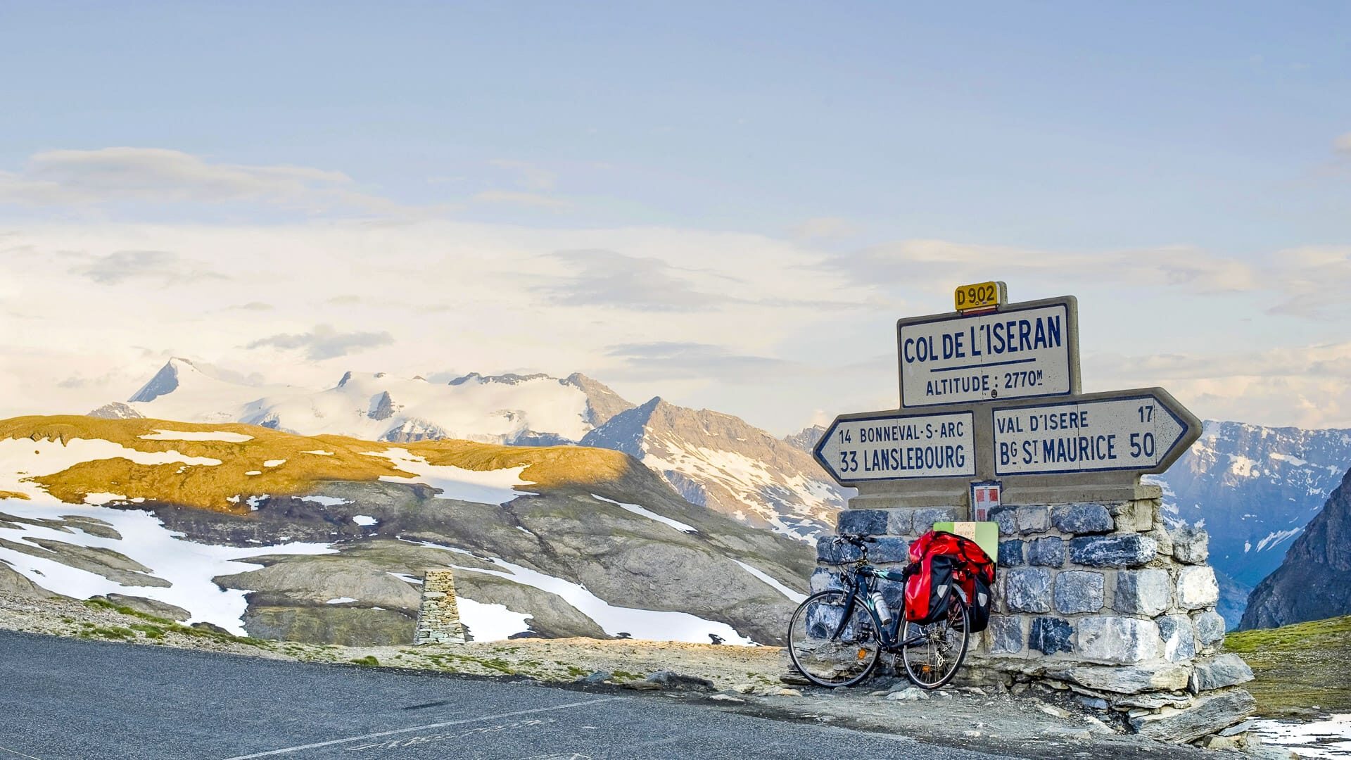 Touring bike by Col de l’Iseran road sign in the French Alps with snowy peaks
