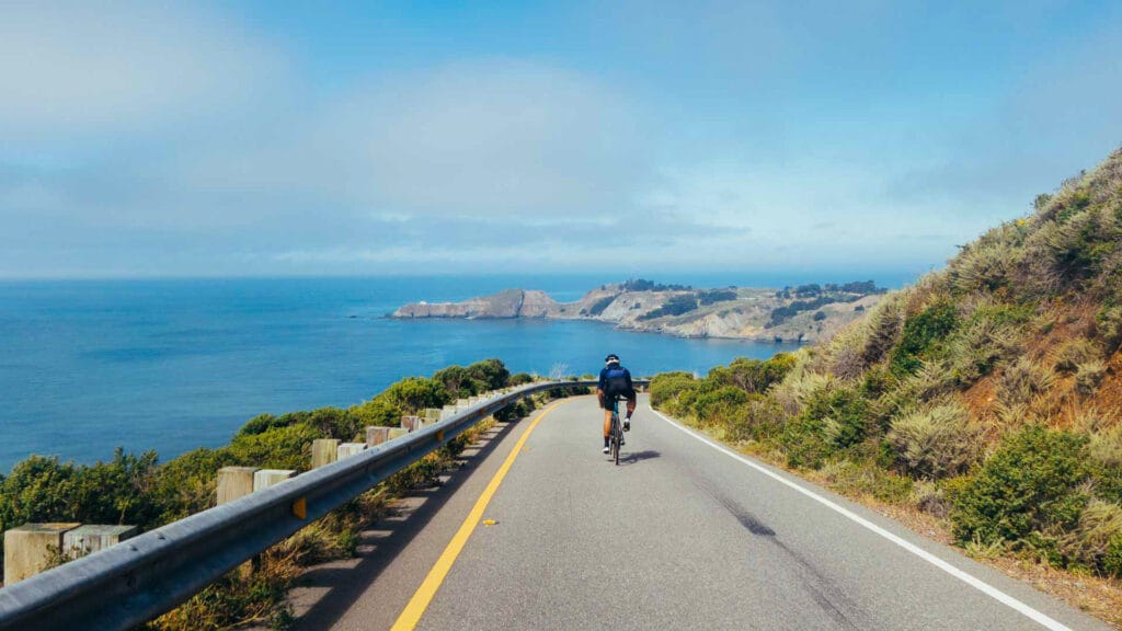 Group of cyclists, teammates, friends, descending windy narrow road next to the bay with fog and water and blue skys san francisco in norhtern california.