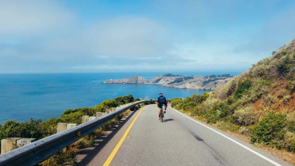 Group of cyclists, teammates, friends, descending windy narrow road next to the bay with fog and water and blue skys san francisco in norhtern california.