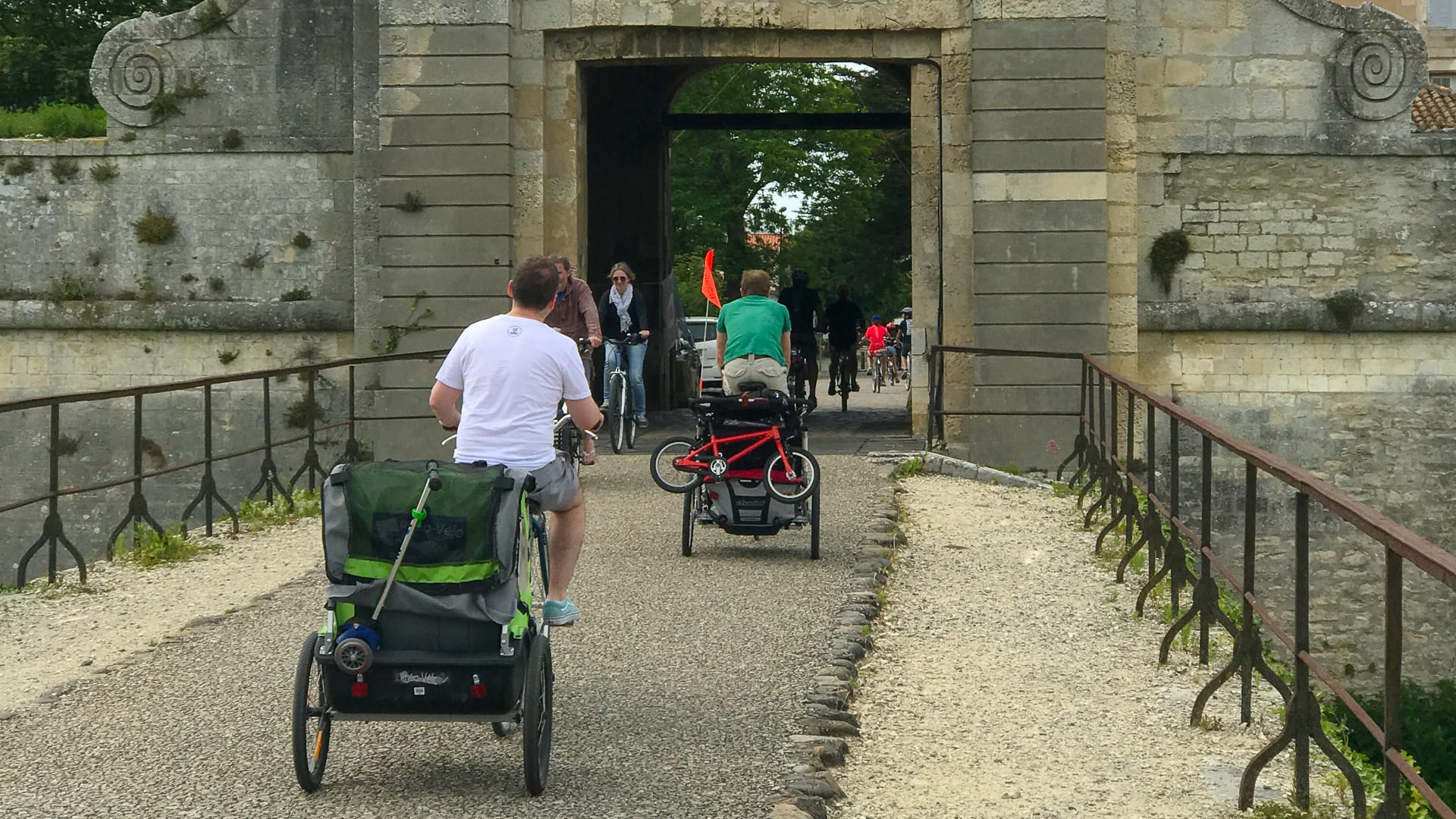 A family cycling towards a large stone gateway