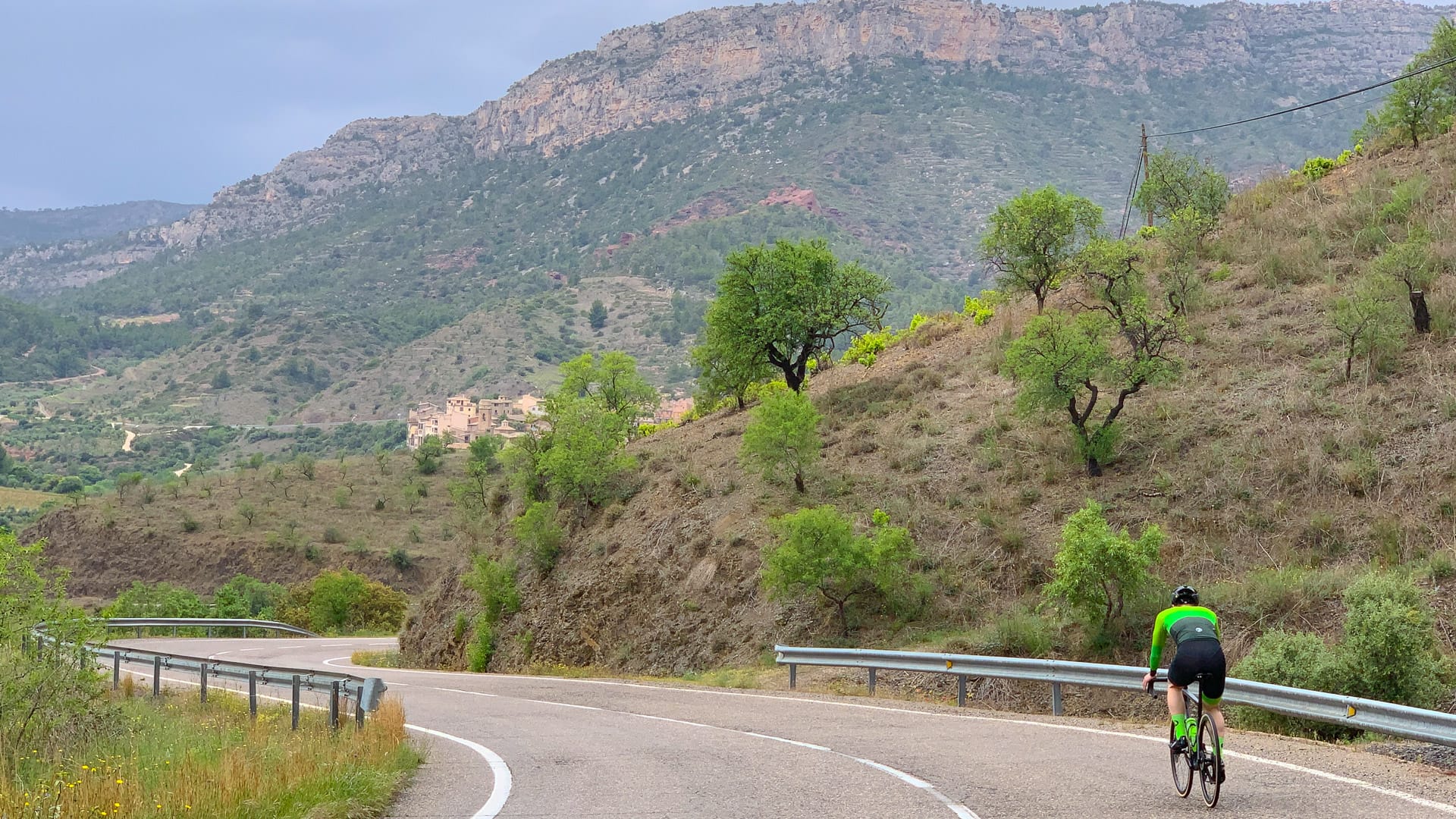 Cyclist climbing a scenic hillside road surrounded by trees and rocky mountains in Tarragona