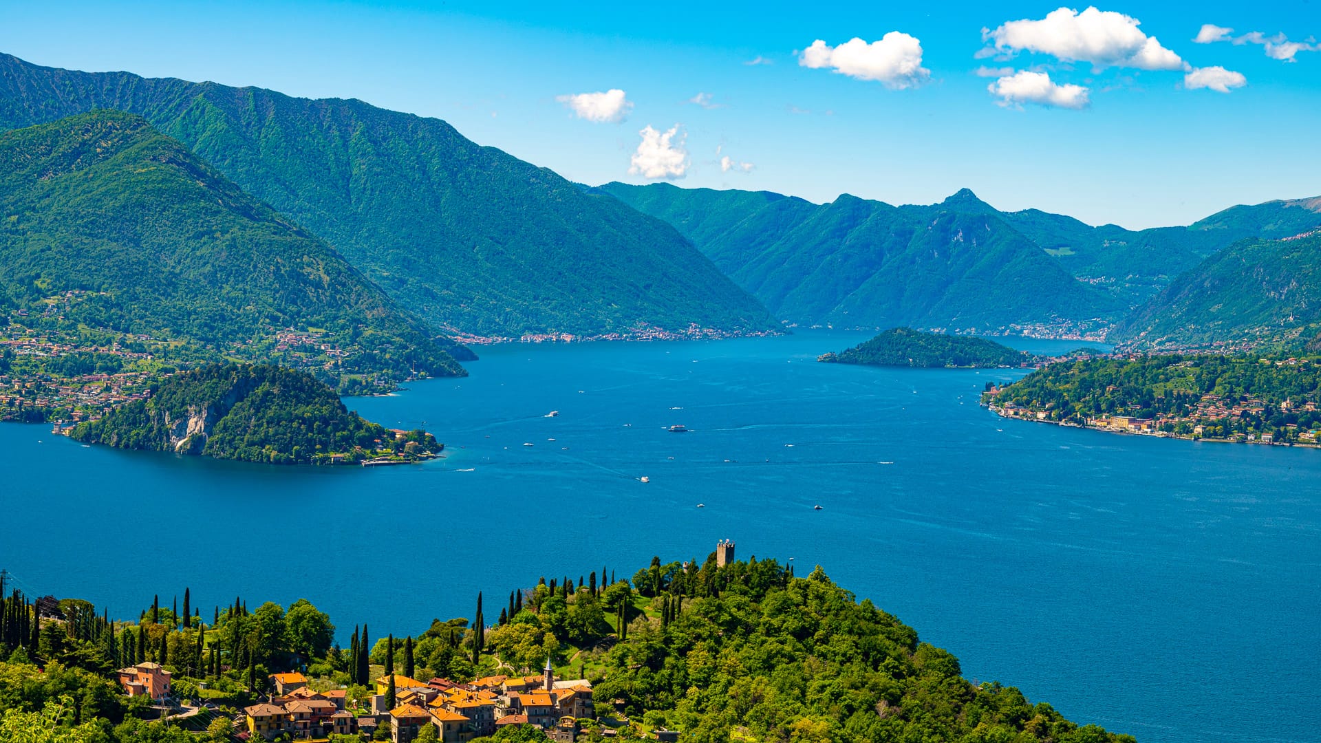Panoramic view of Lake Como from above, showing deep blue water winding between steep green mountains and villages