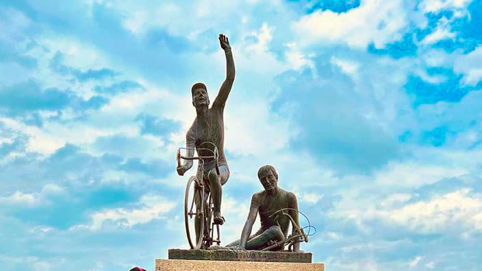 Cycling monument at Madonna del Ghisallo near Lake Como, featuring bronze cyclists under a dramatic sky