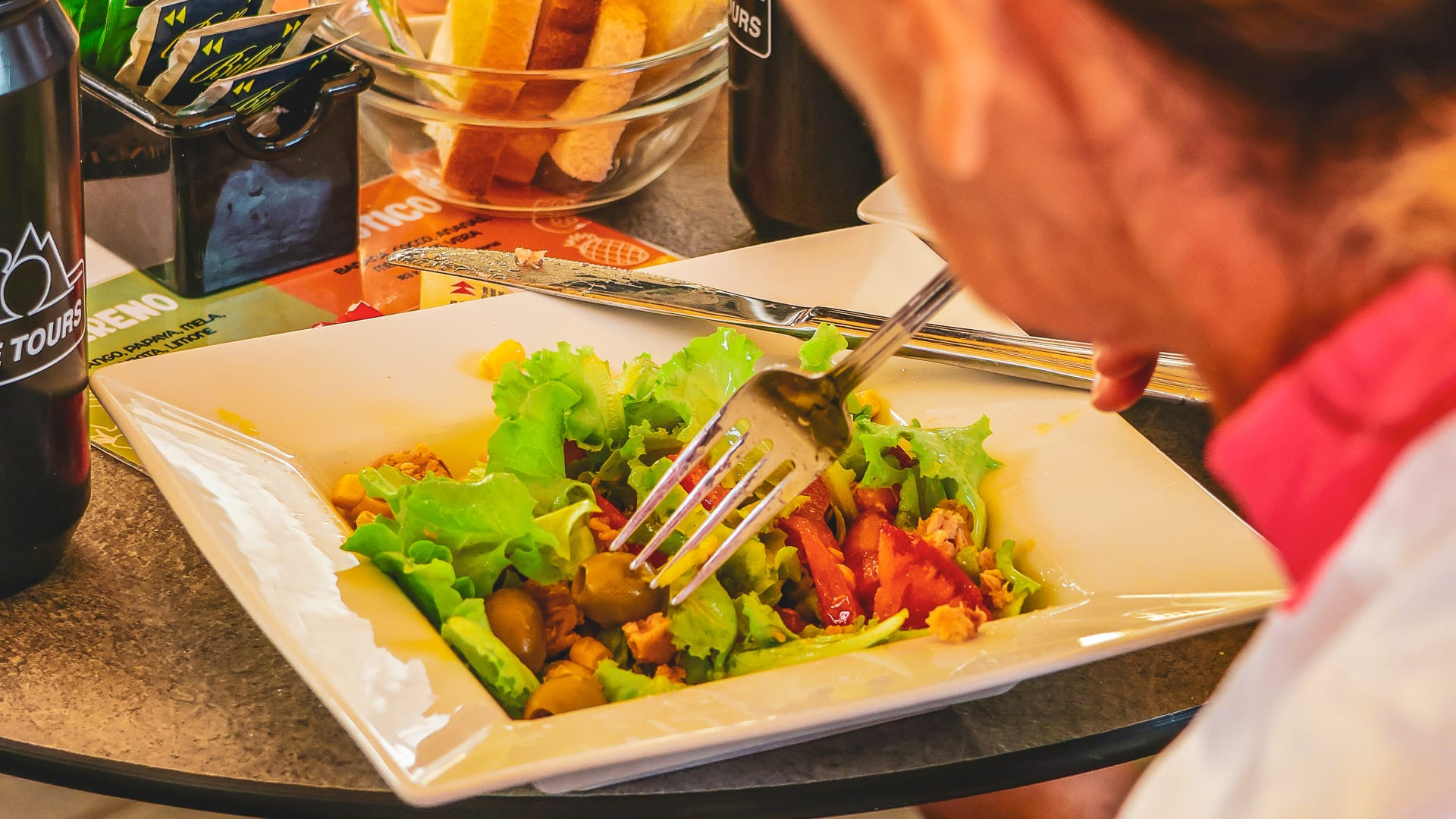 Person enjoying a fresh salad with bread on the table during a cycling tour meal break