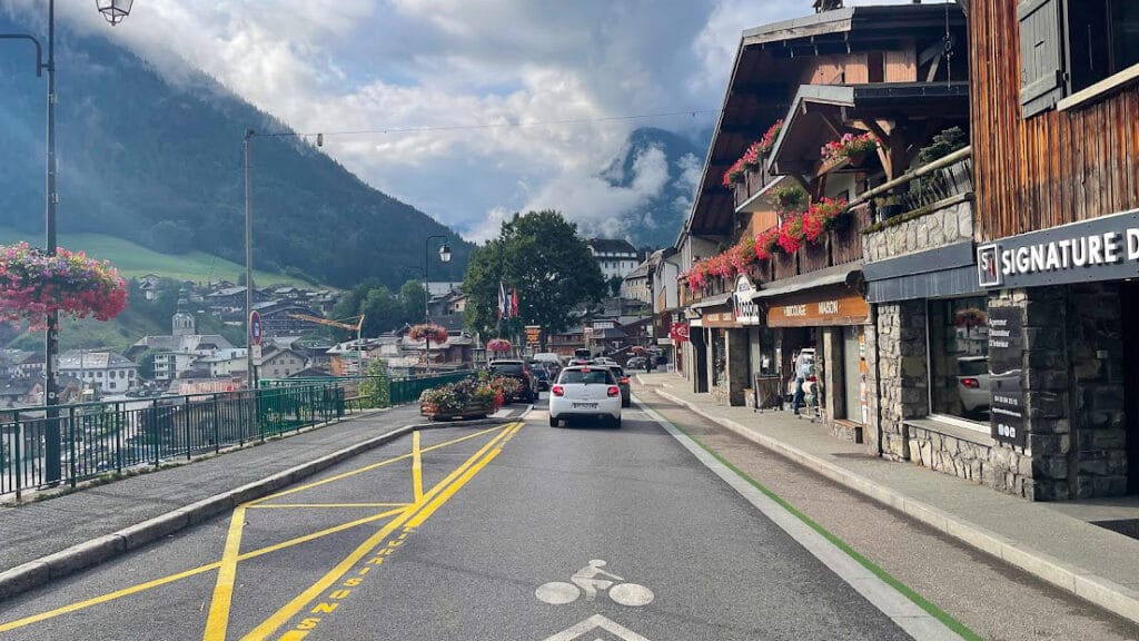 Cycle lane through the centre of Morzine, lined with alpine buildings and flower displays under a cloudy sky