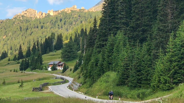 Cyclists riding along a quiet forested road on Passo Campolongo in the Dolomites