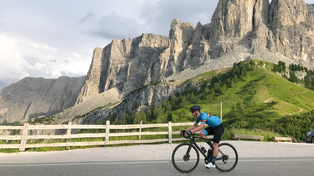 Cyclist riding beneath dramatic rock faces on Passo Gardena in the Dolomites