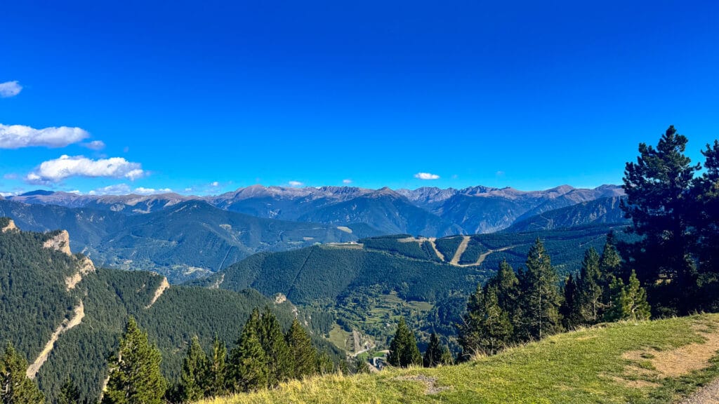 View over La Massana valley, Andorra with forested ridges, ski runs and distant Pyrenean peaks under clear blue sky