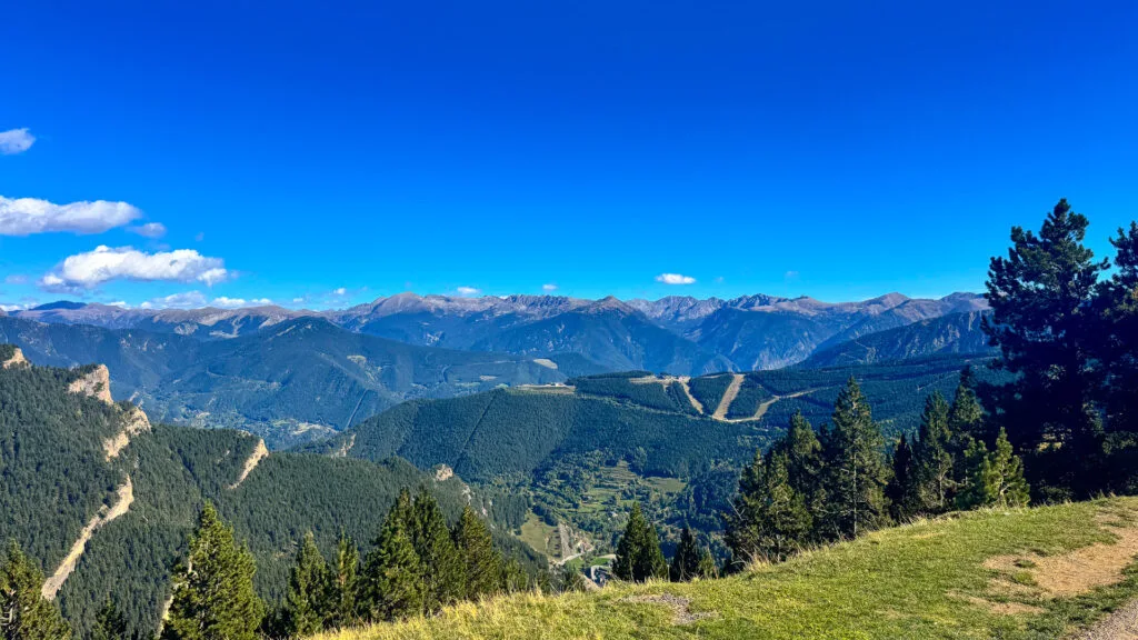 View over La Massana valley, Andorra with forested ridges, ski runs and distant Pyrenean peaks under clear blue sky