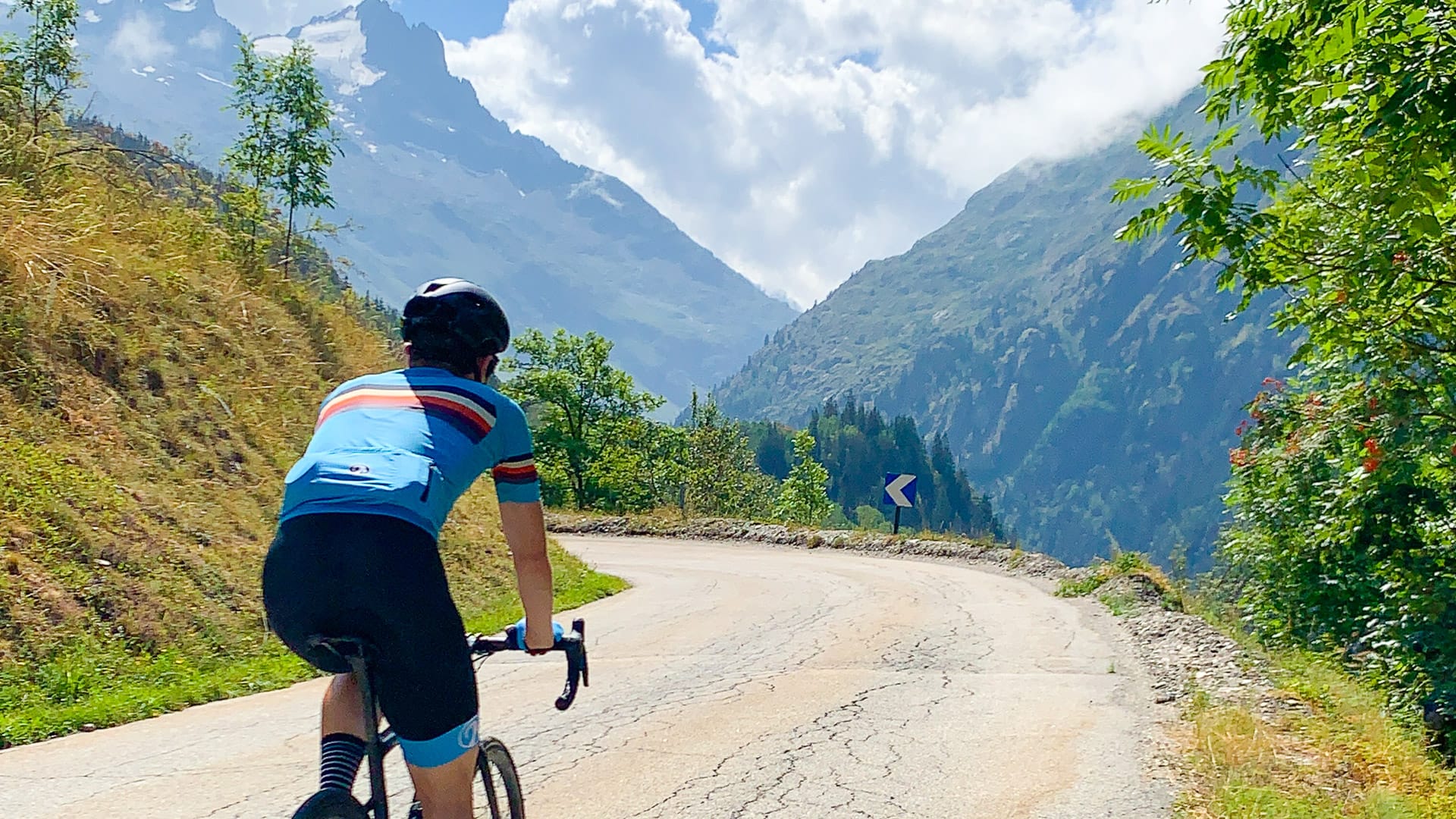 Cyclist climbing remote alpine road with dramatic peaks and clouds in the French Alps