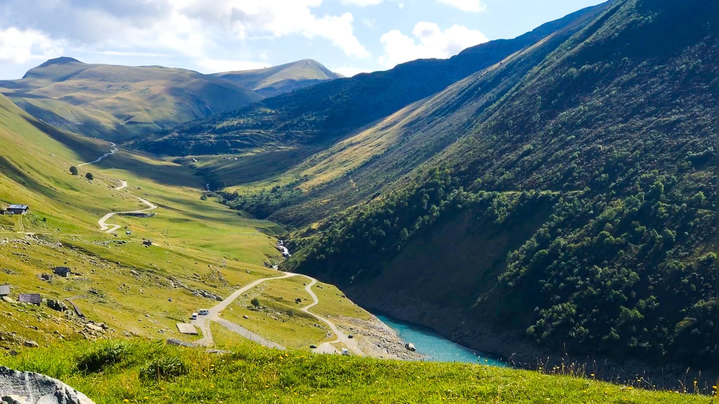 Winding road and reservoir nestled in lush green valley beneath high Pyrenean mountains near Croix de Fer, French Alps