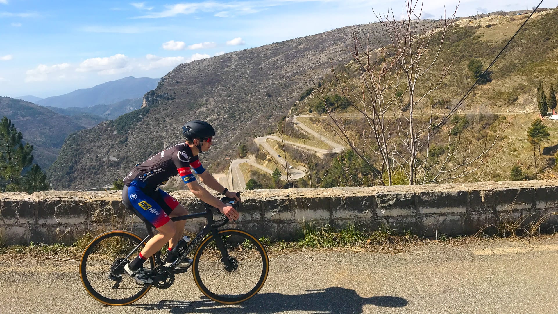 Cyclist riding beside dramatic switchbacks on Col de Braus, French Alps