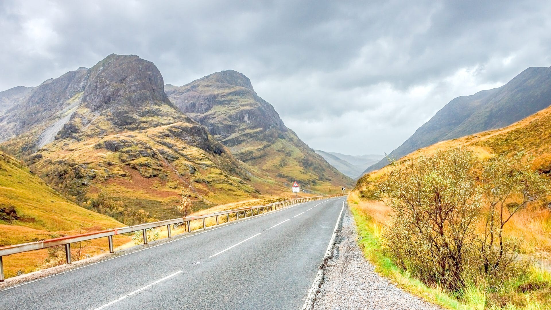 Empty road winding through dramatic mountains and moorland in the Scottish Highlands under stormy skies