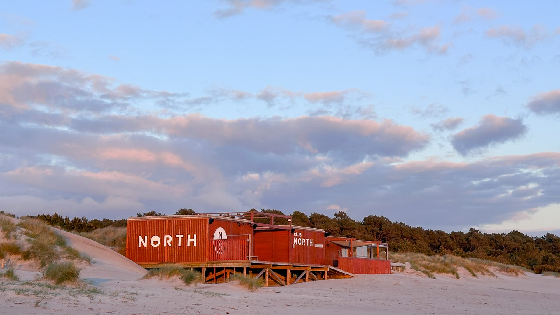 Red North beach bar and restaurant built from containers on sandy dunes at sunset with soft clouds above