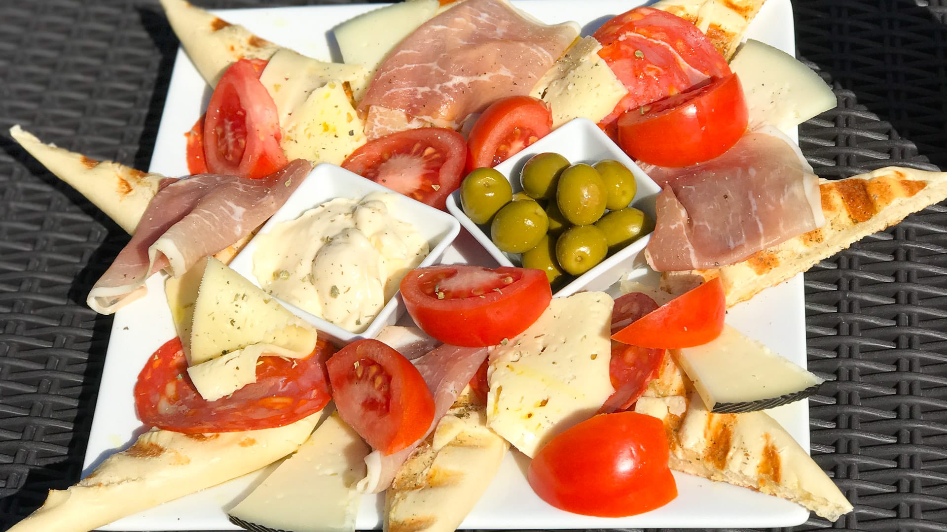 Mediterranean platter with cheese, ham, tomatoes, olives, and bread served on a white plate in Mallorca