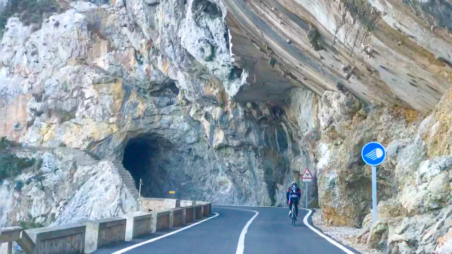 Cyclist riding through rock overhang and tunnel on the Cap de Formentor road, Mallorca