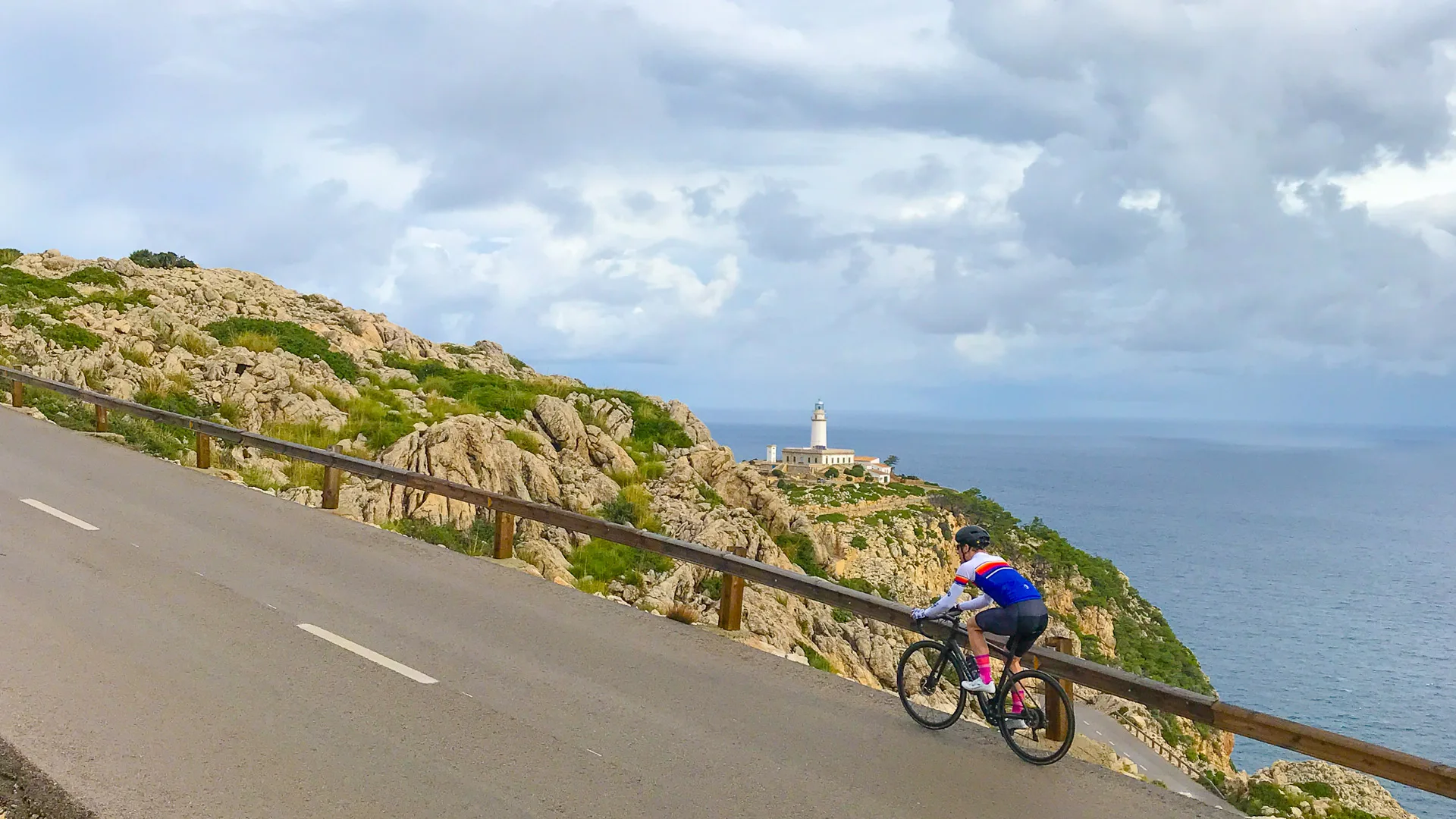 Cyclist cycling the cap de formentor cycling route on Mallorca with lighthouse in distance