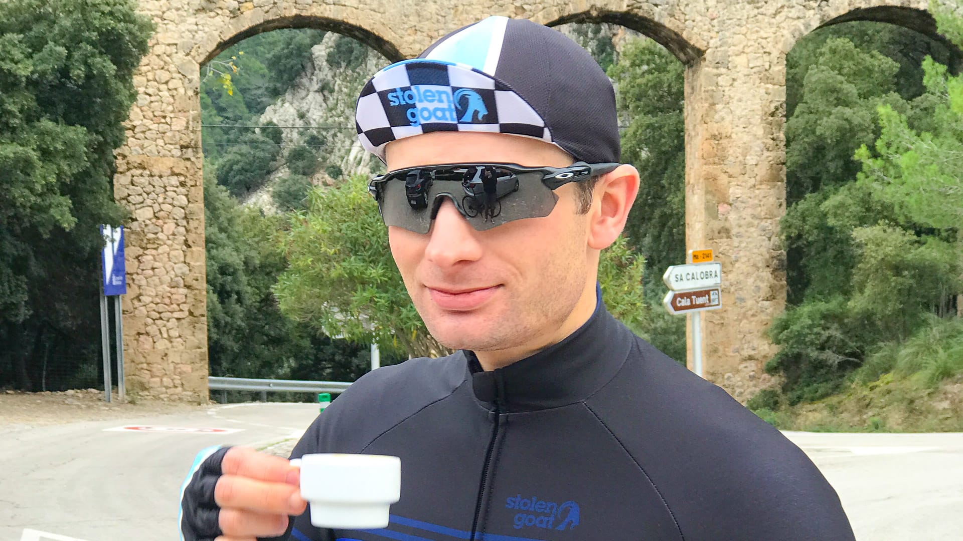 Cyclist enjoying an espresso at Sa Calobra junction beneath the stone aqueduct in Mallorca