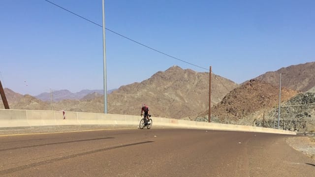 Cyclist climbing a mountain road near Hatta in the Dubai desert with rocky peaks in the background