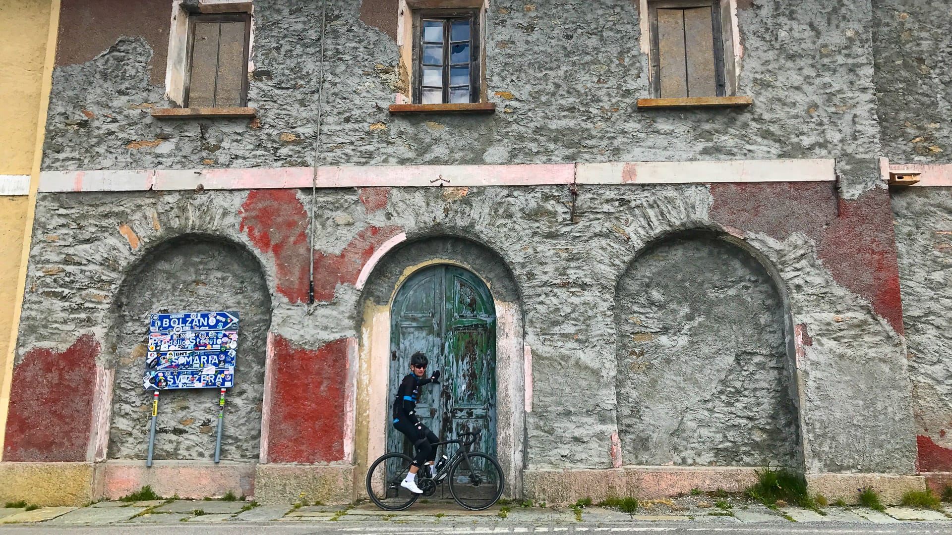Cyclist by old building on way up Stelvio