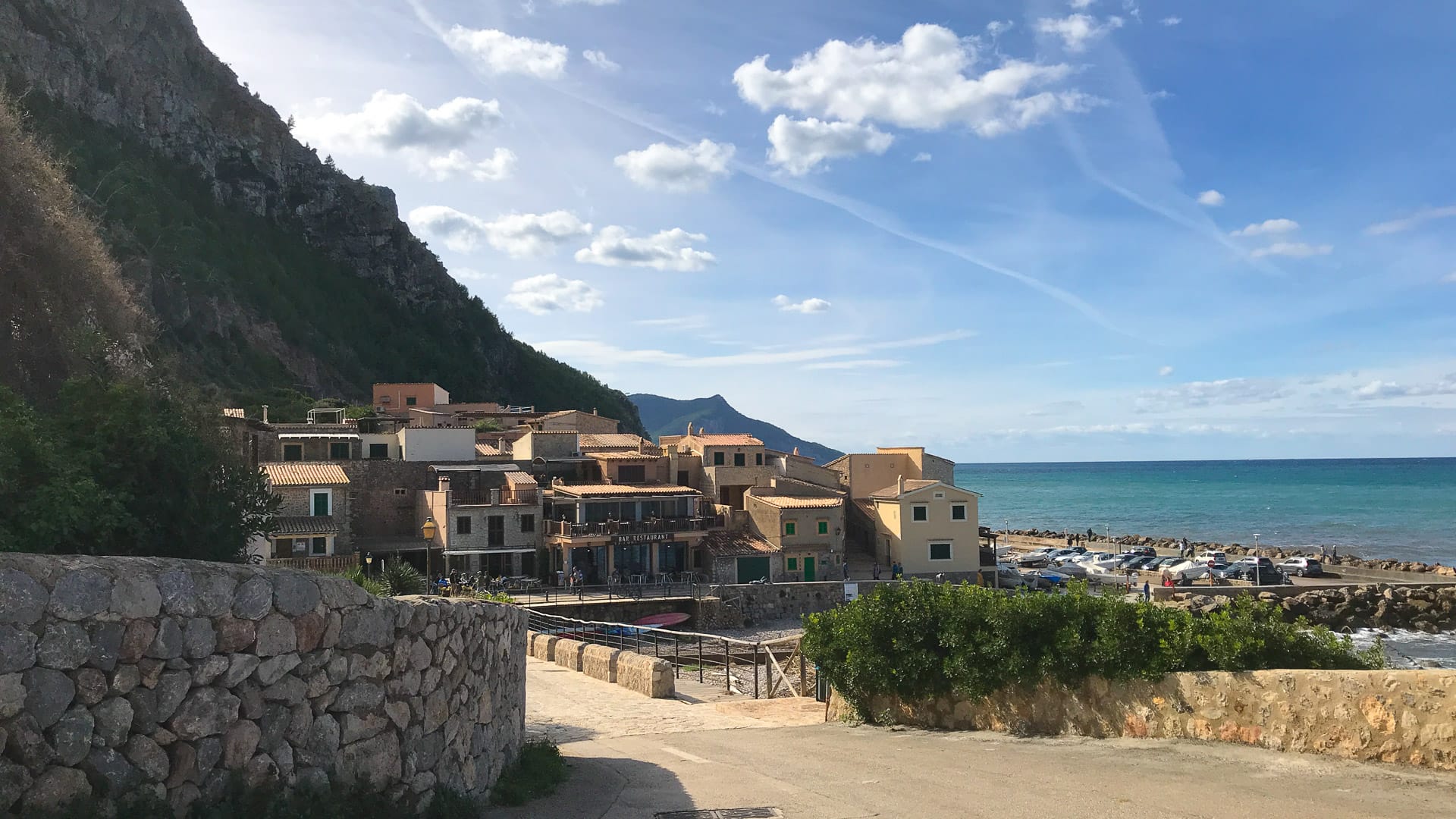 Waterfront buildings and boats at Port de Valldemossa, Mallorca, nestled below steep coastal cliffs on a calm sunny afternoon