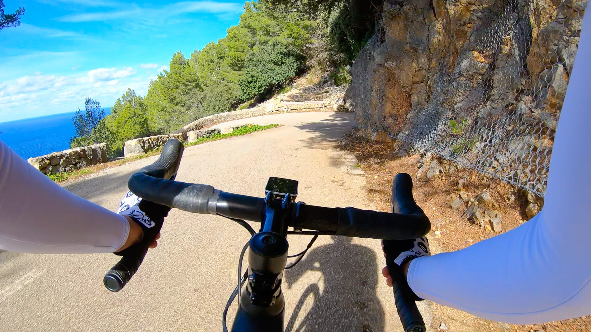 Cyclist’s view on cliffside road above the sea near Port de Valldemossa, Mallorca, with rocky wall and pine forest lining the route