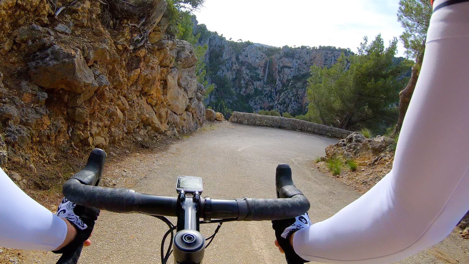 Cyclist’s point of view on narrow winding descent in Mallorca’s Tramuntana range, with stone barrier and steep rocky cliffs ahead