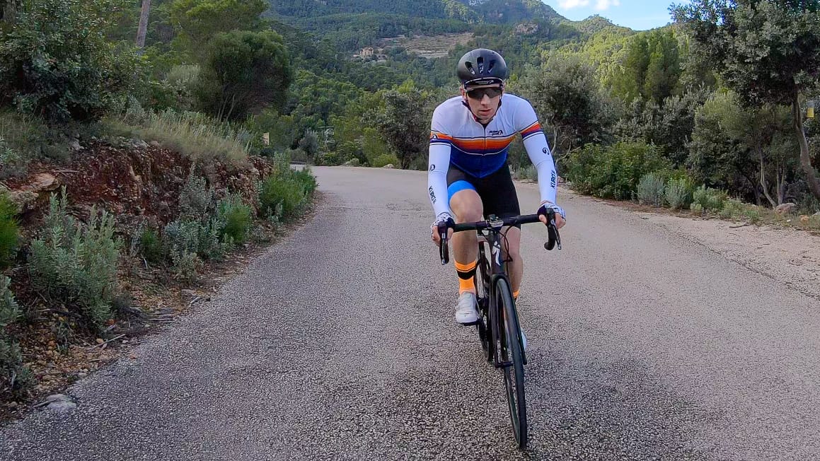Cyclist climbing rural road through forested hills near Port des Canonge, Mallorca