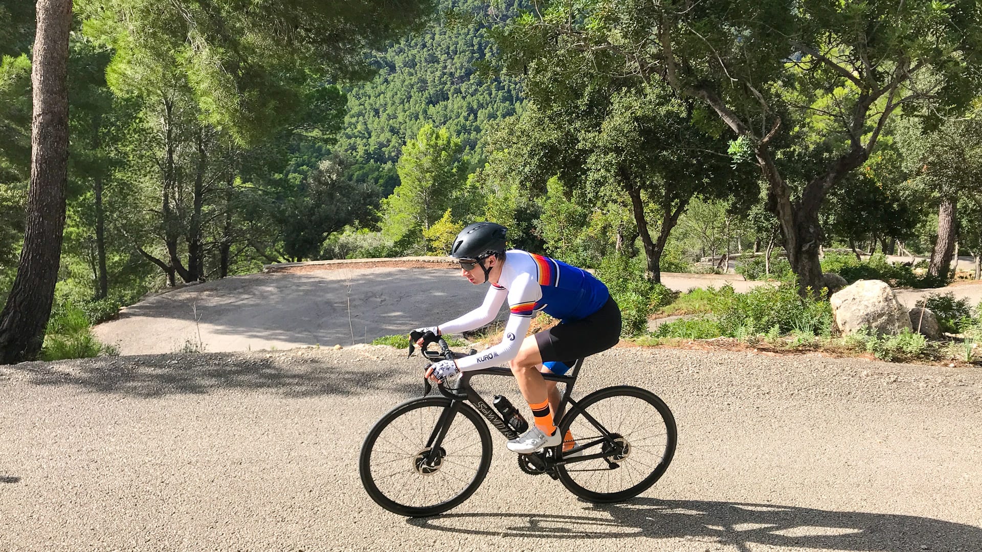 Close-up of cyclist climbing forested switchback road above Port des Canonge, Mallorca
