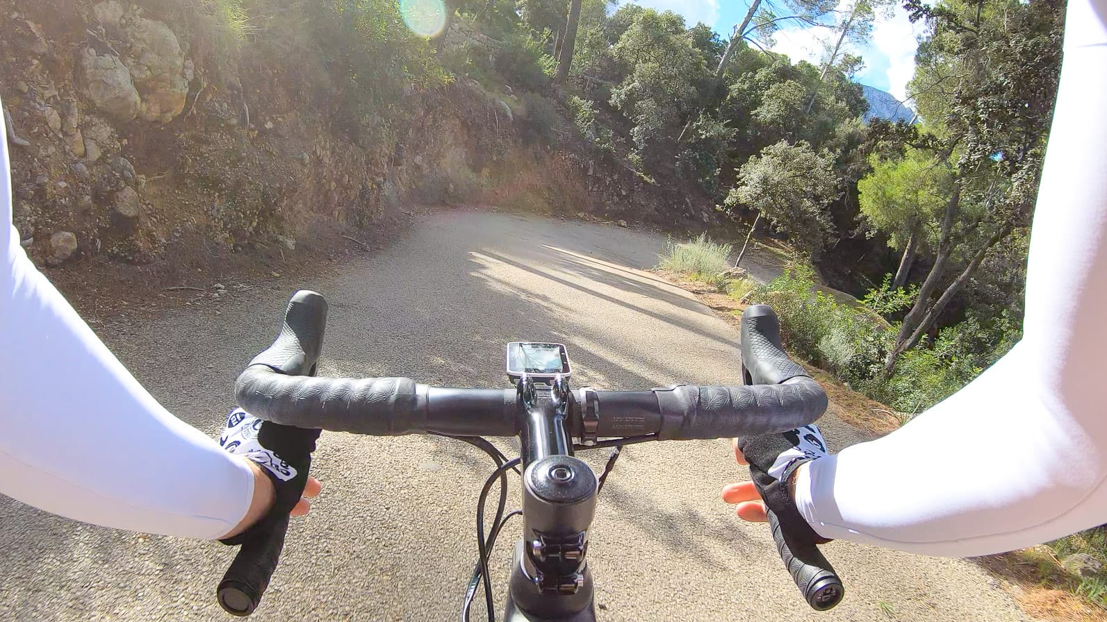 POV of cyclist climbing shaded mountain road near Port des Canonge, Mallorca, with Garmin on handlebars