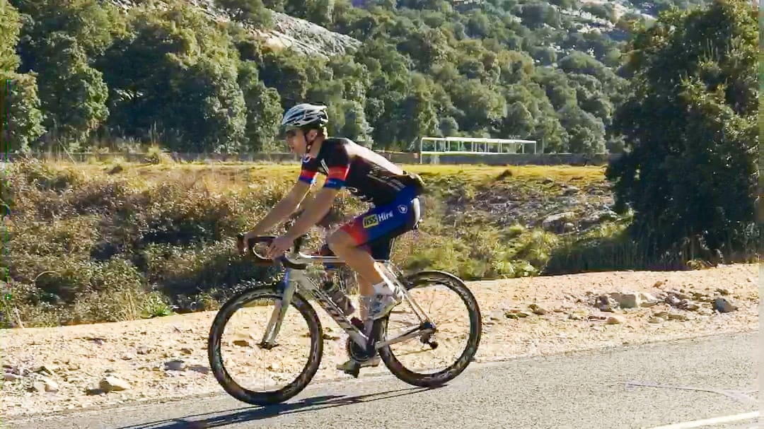 Cyclist riding near Puig Major in Mallorca with forested mountain backdrop under clear skies
