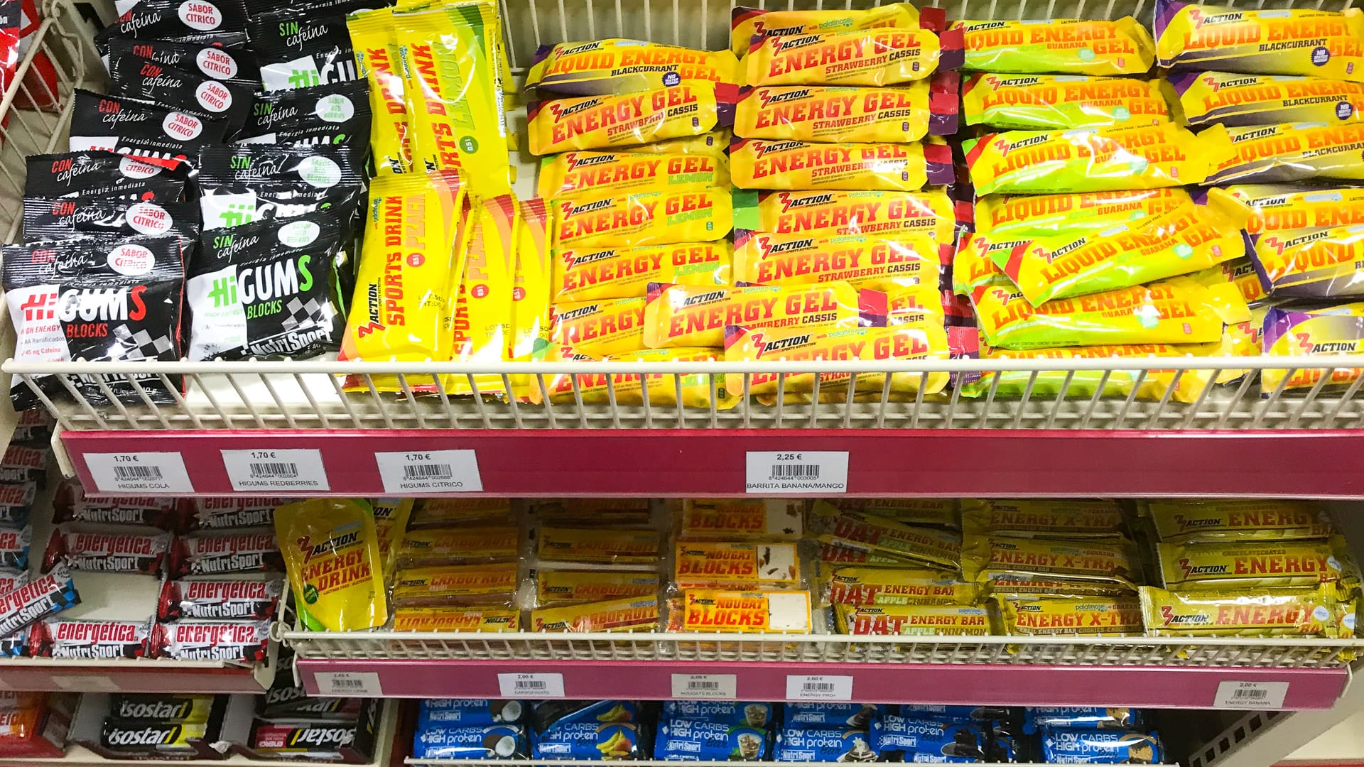 Shelves of energy gels and bars in a sports shop, with bright yellow packaging from brands like PowerBar and Multipower