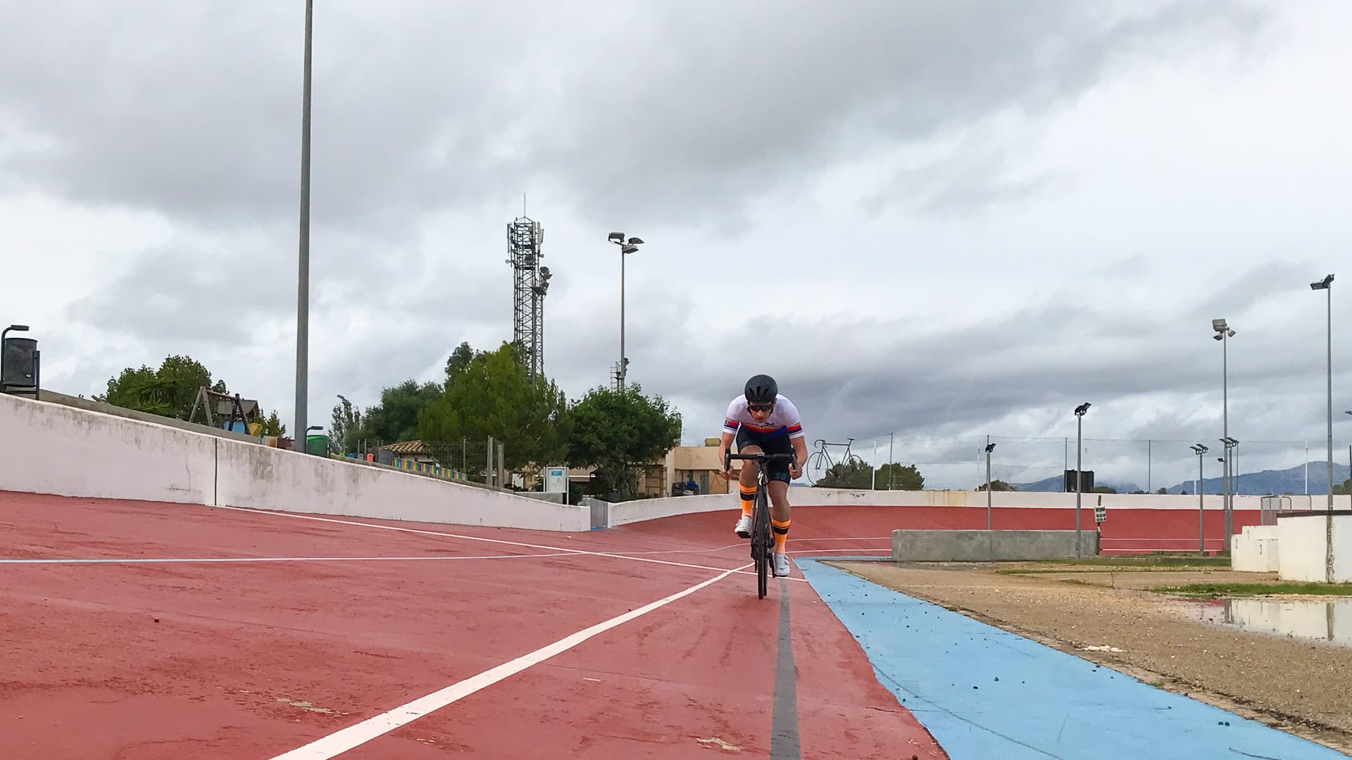 Cyclist riding straight down the velodrome track at Sineu, Mallorca, with cloudy skies and floodlights in the background