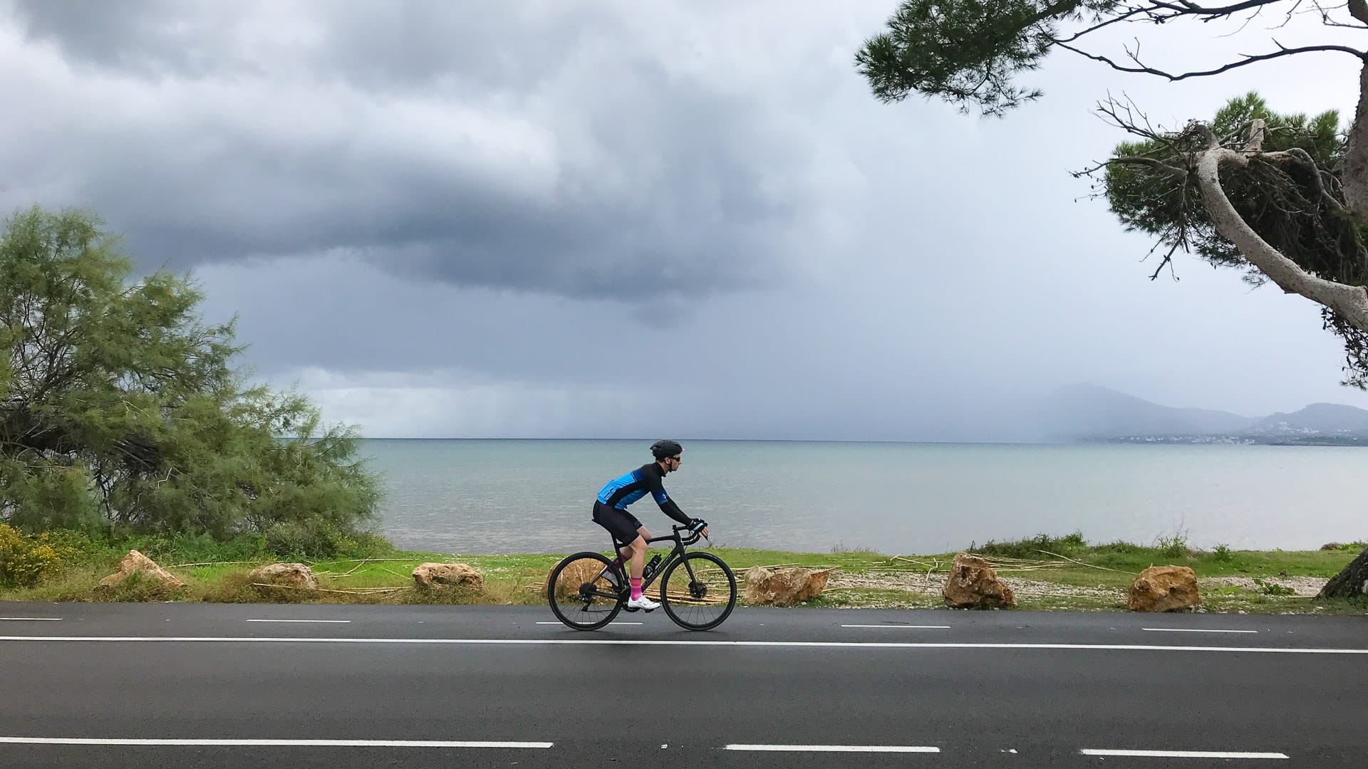 Cyclist cycling around Pollensa bay in rainstorm