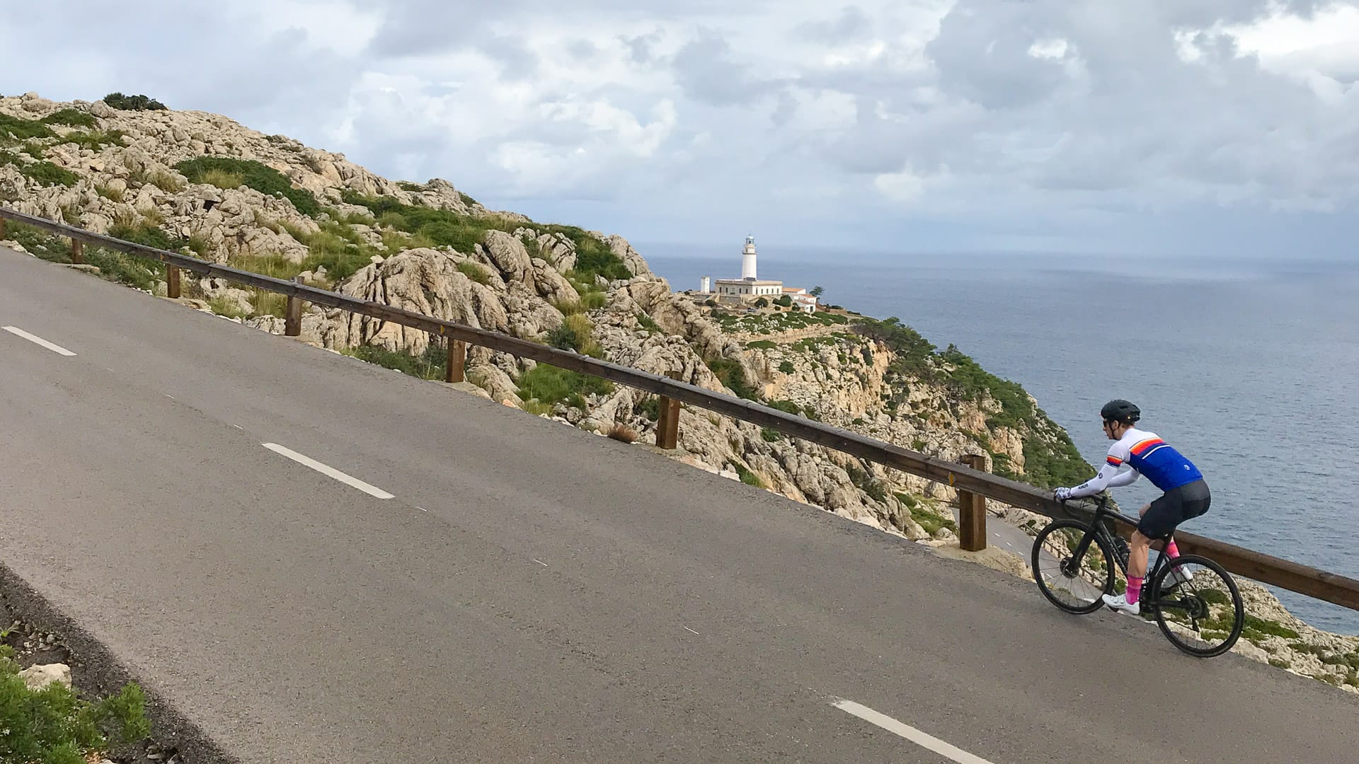 Cyclist cycling the cap de formentor cycling route on Mallorca with lighthouse in distance