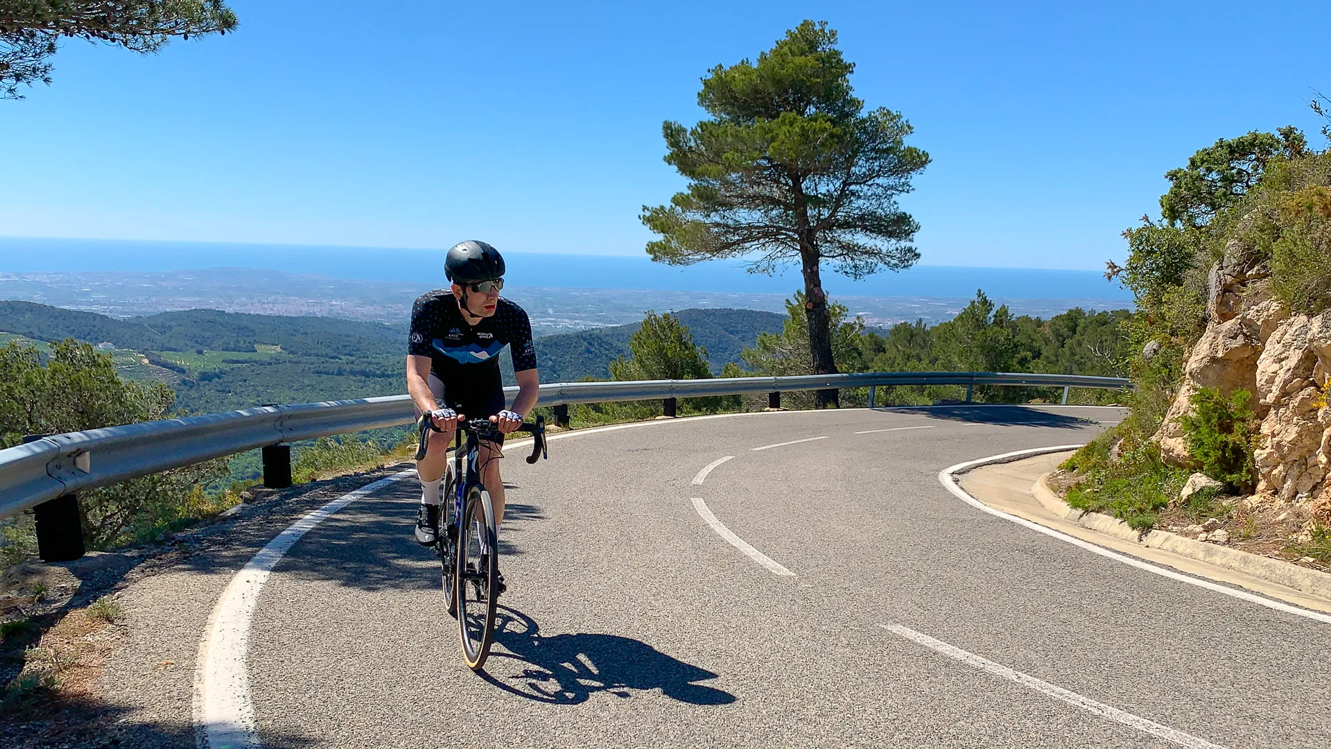 Cyclist climbing a winding mountain road with wide coastal views below on a sunny day